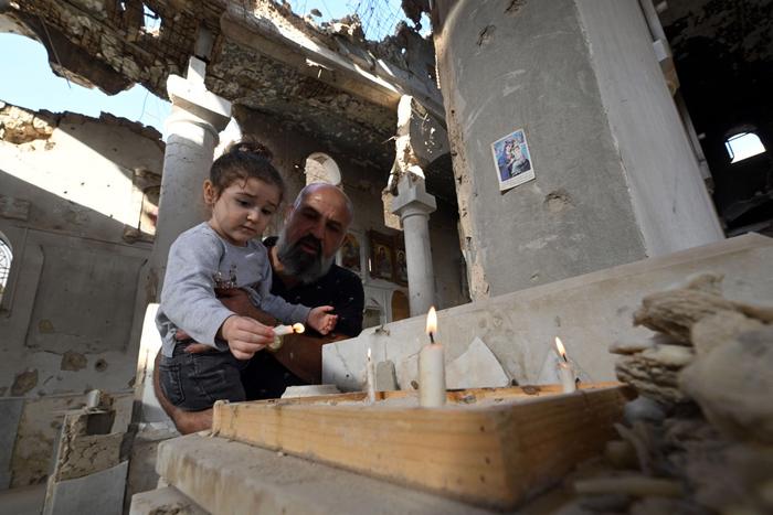 Un chrétien tient sa fille dans ses bras tandis qu'ils allument des bougies sur l'autel de l'église orthodoxe grecque Saint-Takla à Darayya, dans la banlieue de Damas, le 28 octobre 2025.