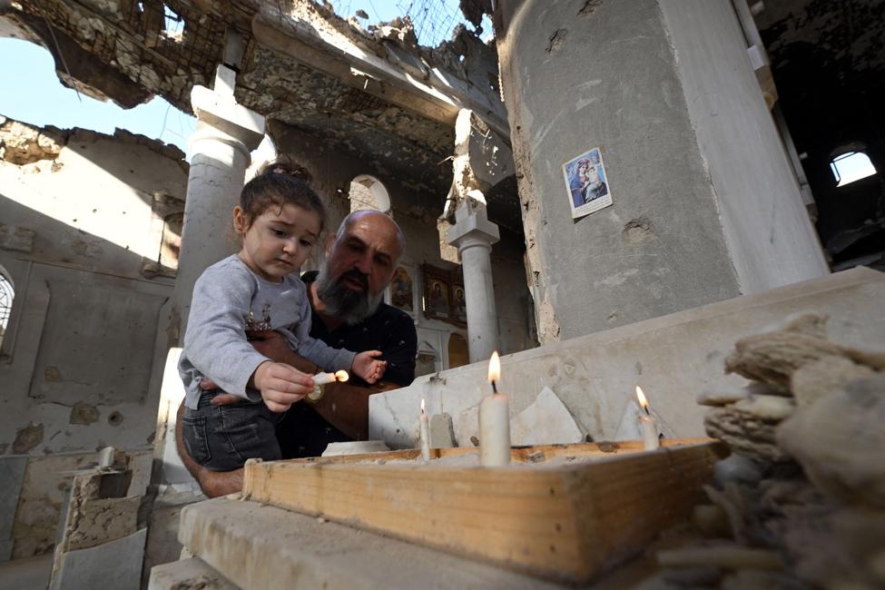 Un chrétien tient sa fille dans ses bras tandis qu'ils allument des bougies sur l'autel de l'église orthodoxe grecque Saint-Takla à Darayya, dans la banlieue de Damas, le 28 octobre 2025.