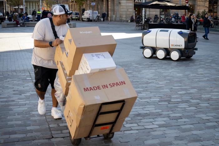 Un homme transportant des colis sur un camion observe le robot de livraison « Ona » se déplaçant dans le centre de Barcelone lors d'un essai pilote, le 22 novembre 2024.