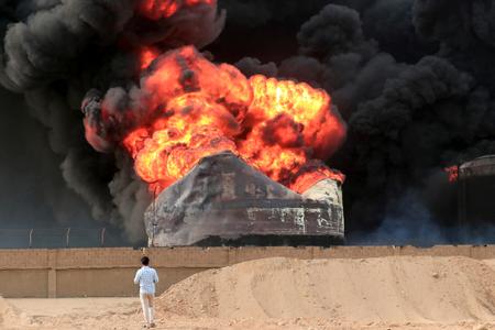 Un homme se tient face à un violent incendie qui ravage des réservoirs de stockage de pétrole, le lendemain des frappes israéliennes sur le port de Hodeida, ville yéménite contrôlée par les Houthis, le 21 juillet 2024.