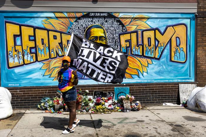 Une femme brandit un drapeau Black Lives Matter devant une fresque de George Floyd près du George Floyd Memorial Square, le 25 mai 2021 à Minneapolis, dans le Minnesota.