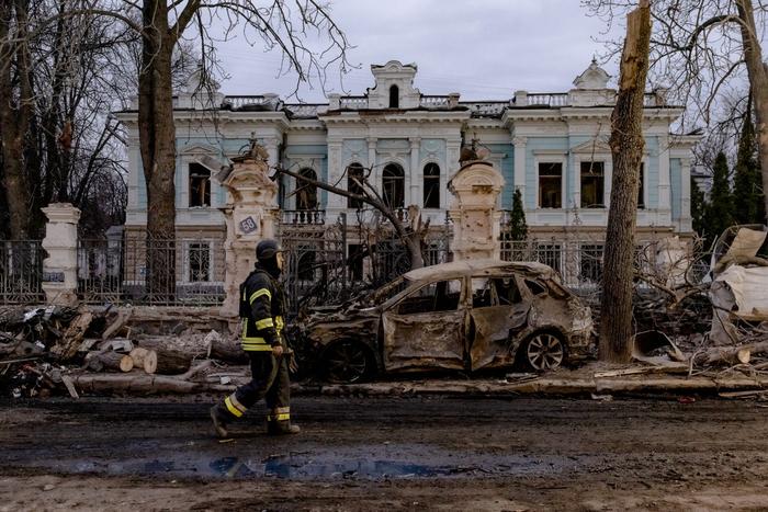 Un sauveteur ukrainien passe devant une voiture brûlée devant un bâtiment endommagé sur le site d'une attaque de missiles à Soumy, dans le nord-est de l'Ukraine, le 13 avril 2025