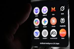 Cette photographie montre un smartphone tenu à la main, sur l’écran duquel apparaissent les icônes de certaines des principales applications reposant sur l’intelligence artificielle, notamment des grands modèles de langage (LLM), des agents conversationnels et des outils d’IA générative. On distingue, de gauche à droite, les logos de Lumo (Proton AG), Meta AI, Mistral Vibe (anciennement Le Chat), Grok (xAI), Copilot (Microsoft), Gemini (Google), Claude (Anthropic), Perplexity, DeepSeek, ChatGPT (OpenAI), NotebookLM (Google) et Suno, une application de génération musicale par IA.