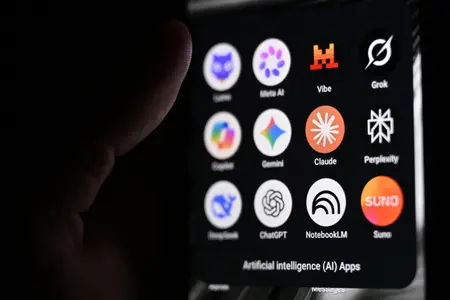 Cette photographie montre un smartphone tenu à la main, sur l’écran duquel apparaissent les icônes de certaines des principales applications reposant sur l’intelligence artificielle, notamment des grands modèles de langage (LLM), des agents conversationnels et des outils d’IA générative. On distingue, de gauche à droite, les logos de Lumo (Proton AG), Meta AI, Mistral Vibe (anciennement Le Chat), Grok (xAI), Copilot (Microsoft), Gemini (Google), Claude (Anthropic), Perplexity, DeepSeek, ChatGPT (OpenAI), NotebookLM (Google) et Suno, une application de génération musicale par IA.