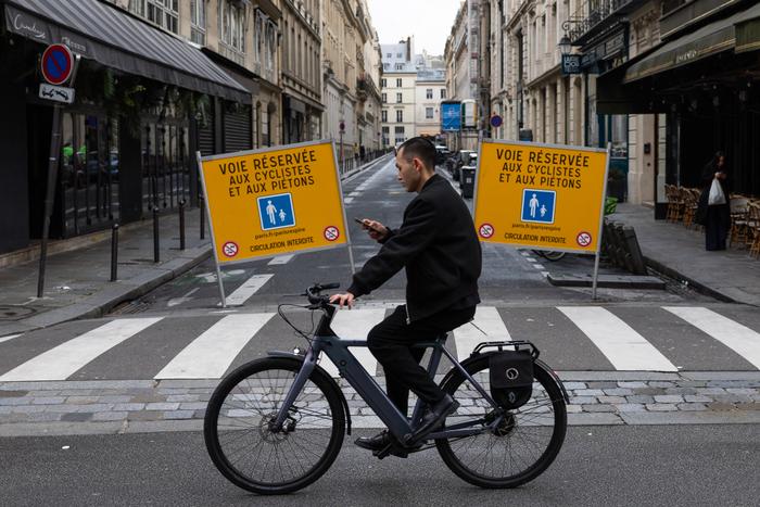 Un homme consulte son téléphone portable alors qu'il conduit un vélo électrique et franchit des barrières signalant la voie réservée aux piétons et aux cyclistes, à Paris, le 9 février 2025.