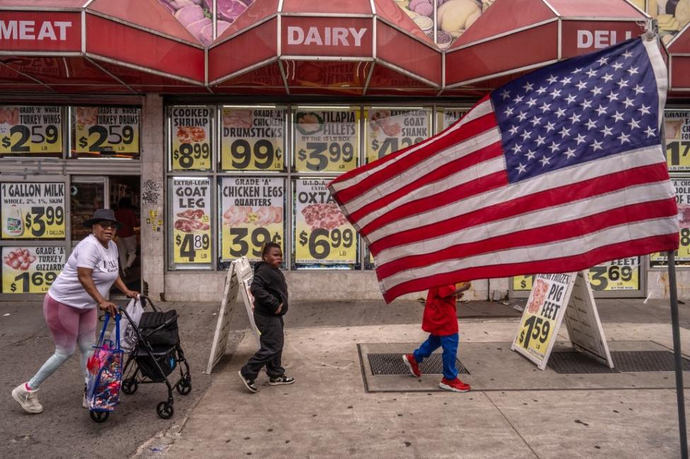 Des gens passent devant le drapeau des États-Unis dans le quartier de Little Haiti, le 8 juin 2025, dans l'arrondissement de Brooklyn à New York.