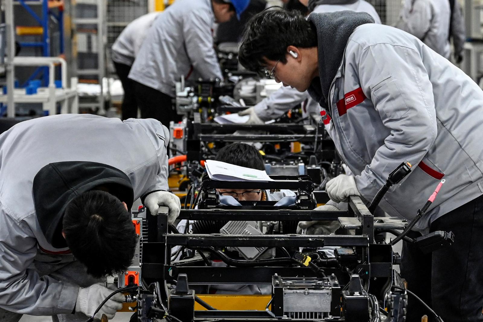 Cette photo, prise le 4 décembre 2025, montre des employés travaillant sur une chaîne de production de véhicules Neolix X3 dans une usine du constructeur chinois de véhicules de livraison autonomes Neolix, à Yancheng, dans la province du Jiangsu, en Chine orientale. Dans un atelier lumineux de l'est de la Chine, un bras robotisé déplace un véhicule autonome partiellement assemblé tandis que des ouvriers calibrent ses caméras. Cette opération est typique de l'automatisation progressive adoptée même dans les plus petites usines de cette puissance industrielle mondiale.