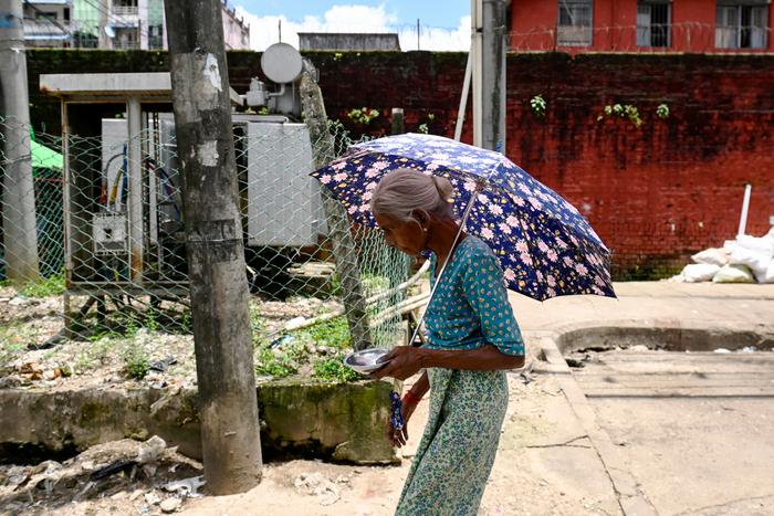 Une femme âgée marche sous un parapluie pour se protéger du soleil par forte chaleur à Yangon, le 13 août 2025.
