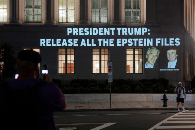 Des personnes prennent en photo une image du président américain Donald Trump et de Jeffrey Epstein, projetée sur le siège du ministère américain du Commerce, le 18 juillet 2025, à Washington.