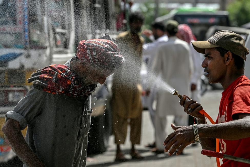 Un bénévole de la Fondation Edhi pulvérise de l'eau sur la tête d'un passant pour se rafraîchir lors d'une chaude journée d'été le long d'une route au milieu de la vague de chaleur à Karachi le 21 avril 2025.