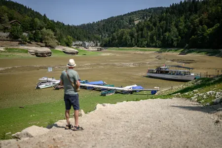 Un touriste fait face au lit asséché du lac des Brenets, qui fait partie du Doubs, une frontière naturelle entre l'est de la France et l'ouest de la Suisse, alors que l'Europe centrale est frappée par une nouvelle vague de chaleur, aux Brenets le 11 août 2026.