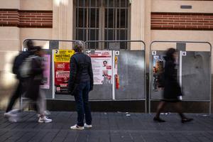 Des piétons passent devant un panneau avec les affiches de campagne des candidats à la mairie de Toulouse pour les prochaines élections municipales, le 10 mars 2026.