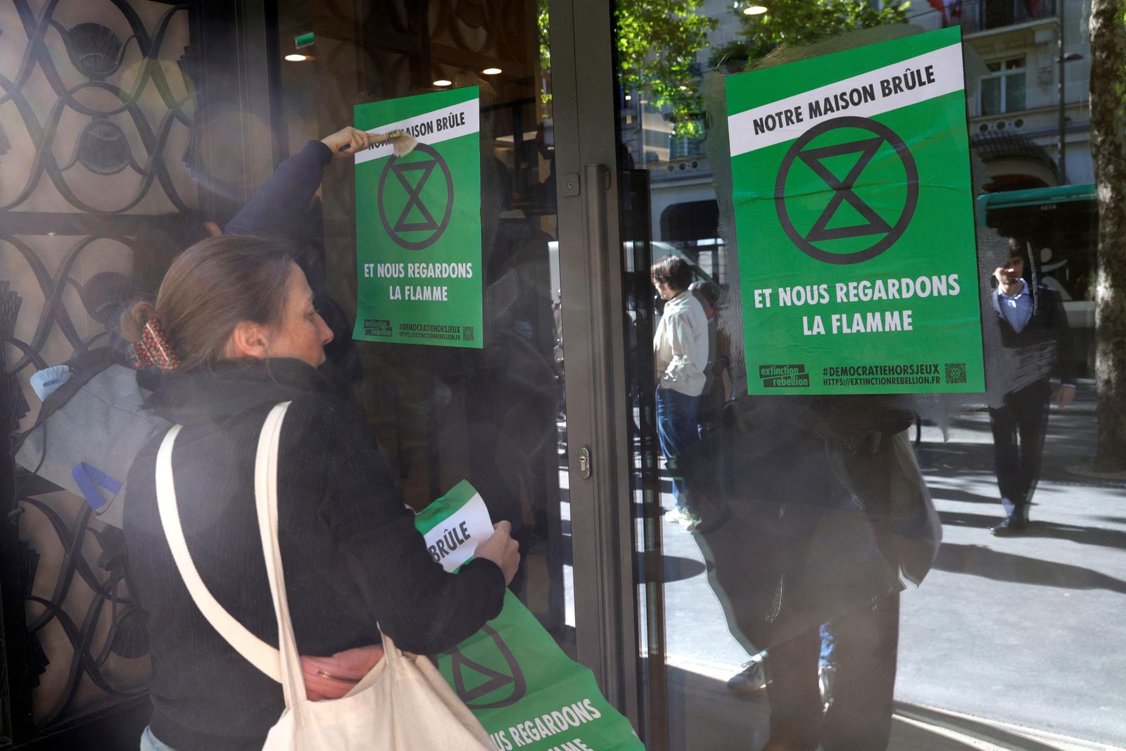 Des membres d'Extinction Rebellion collent des affiches lors d'une manifestation devant les bureaux de la banque BNP Paribas, en amont de l'assemblée générale des actionnaires de TotalEnergies, à Paris, le 23 mai 2025.