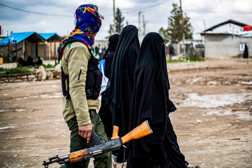 Des femmes étrangères, vivant dans le camp d'al-Hol qui abrite des proches de membres du groupe État islamique (EI), marchent sous la surveillance d'un combattant des Forces démocratiques syriennes (FDS) dans le nord-est de la Syrie.