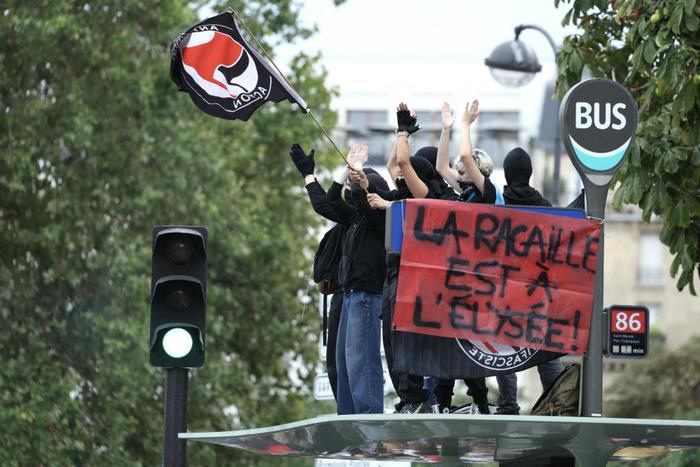 Des manifestants brandissent un drapeau antifasciste à côté d'une pancarte sur laquelle on peut lire « la racaille est à l'Élysée », à Paris, le 7 septembre 2024.