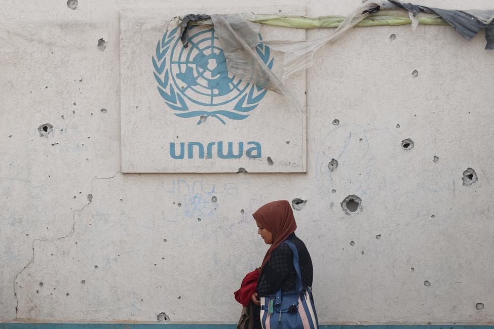 Une Palestinienne passe devant un mur endommagé affichant le logo de l'UNRWA dans un camp de déplacés à Rafah, dans le sud de la bande de Gaza, le 28 mai 2024.