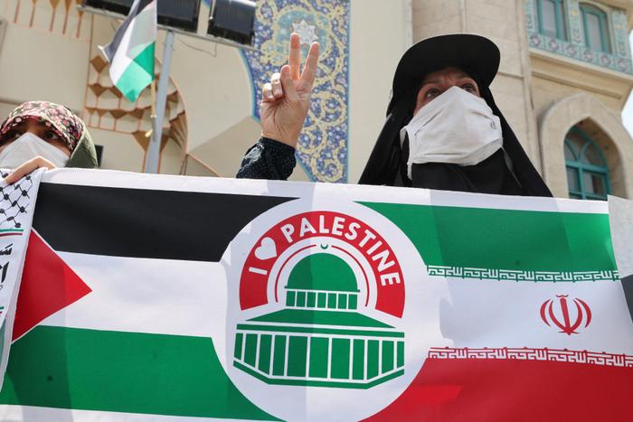 Une manifestante iranienne se tient derrière une banderole fusionnant les drapeaux nationaux palestinien et iranien à Téhéran, le 18 mai 2021.