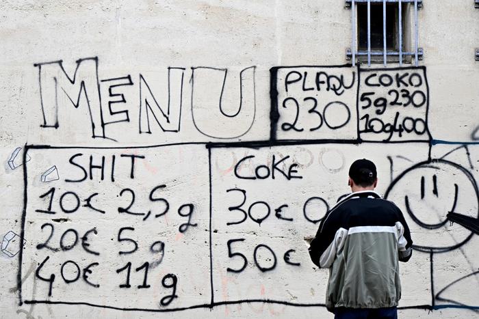 Un homme se tient devant le « menu » de différentes drogues vendues par des dealers, tagué sur la façade d'un immeuble d'un quartier d'Avignon, dans le sud de la France, le 13 mars 2025.