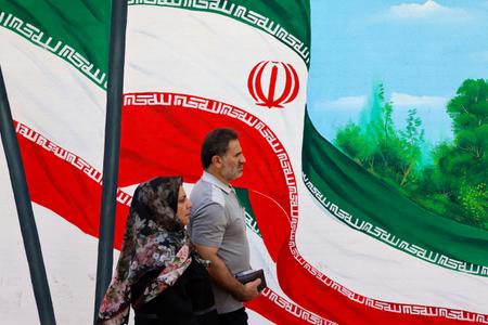 Un homme et une femme passent devant une fresque représentant des drapeaux nationaux iraniens dans une rue de Téhéran, le 20 août 2024. (Image d'illustration)