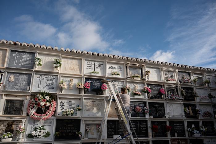 Une femme dépose des fleurs et nettoie une niche funéraire dans un cimetière. (Image d'illustration)