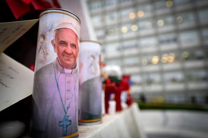Une bougie avec un portrait du pape François est placée au pied d'une statue du pape Jean-Paul II à l'extérieur de l'hôpital Gemelli de Rome, le 19 février 2025.