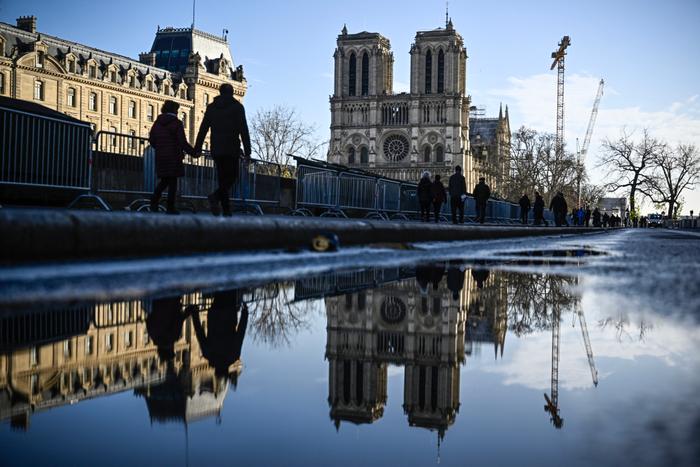 Des piétons passent devant les barrières de sécurité et les grillages placés autour de la cathédrale Notre-Dame de Paris, le 6 décembre 2024.