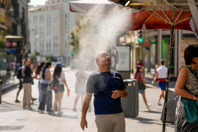 Un homme passe sous un brumisateur rafraîchissant devant un kiosque, alors que les températures grimpent en flèche lors d'une vague de chaleur à Madrid, le 5 août 2025.