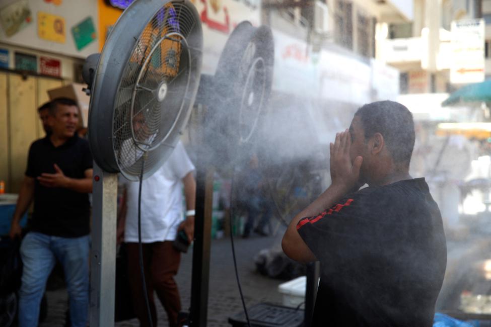 Un homme se rafraîchit devant des « ventilateurs de pulvérisation d'eau » placés sur le bord de la route alors que les températures montent en flèche dans la ville de Bagdad, en Irak, le 30 juin 2024.