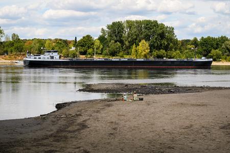 Un navire longe le lit partiellement asséché du Rhin, à hauteur du parc énergétique et chimique Shell Rheinland-Nord, à Godorf, près de Cologne, dans l’ouest de l’Allemagne, le 7 août 2026, après une période de chaleur exceptionnelle. La production industrielle et les exportations allemandes ont légèrement progressé en juin, a indiqué vendredi l’Office fédéral de la statistique, mais les analystes mettent en garde contre les risques liés à l’assèchement des cours d’eau et à la guerre au Moyen-Orient. (Image d'illustration)