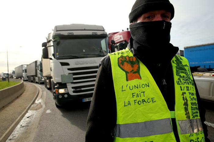 Un manifestant portant un gilet jaune se tient devant des camions bloquant l'autoroute lors d'une manifestation, à Reims, dans le nord de la France, le 20 mars 2023.