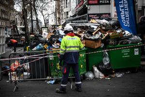 Un employé municipal se tient à côté d'un tas d'ordures avant de le ramasser avec une pelleteuse mobile sur un trottoir à Paris.
