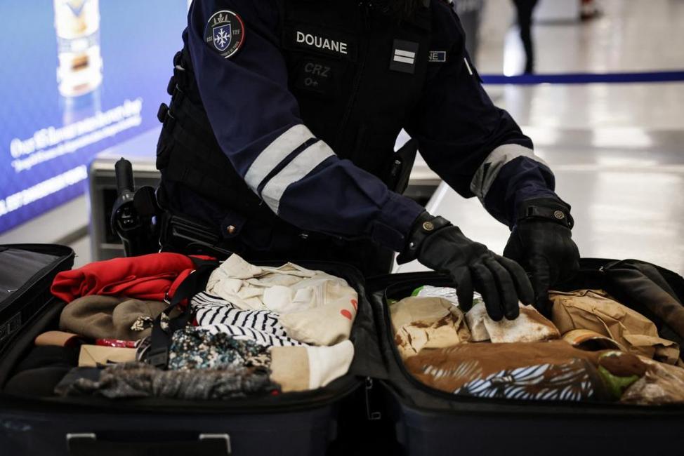 Un agent des douanes françaises contrôle une valise d'un voyageur à l'aéroport Roissy-Charles de Gaulle.