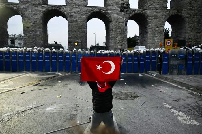Un manifestant tient un drapeau turc devant des policiers lors d'un rassemblement en soutien au maire d'Istanbul arrêté dans la municipalité d'Istanbul, le 23 mars 2025.
