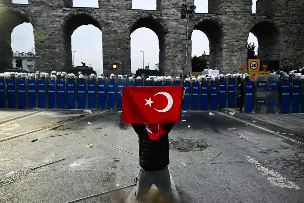 Un manifestant tient un drapeau turc devant des policiers lors d'un rassemblement en soutien au maire d'Istanbul arrêté dans la municipalité d'Istanbul, le 23 mars 2025.
