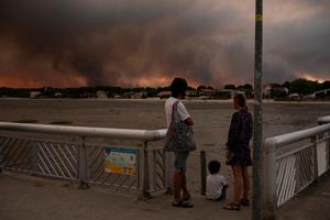 Cette photo montre des personnes observant la fumée depuis la plage d'Andernos-les-Bains lors d'un incendie dans la forêt de Lège-Cap-Ferret, dans le sud-ouest de la France, le 23 juillet 2026, alors qu'une partie de la zone avoisinante a été évacuée.