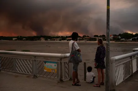Cette photo montre des personnes observant la fumée depuis la plage d'Andernos-les-Bains lors d'un incendie dans la forêt de Lège-Cap-Ferret, dans le sud-ouest de la France, le 23 juillet 2026, alors qu'une partie de la zone avoisinante a été évacuée.