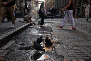 Des pigeons se baignent dans une flaque d'eau tandis que des passants circulent sur Wall Street, devant le siège de la Bourse de New York (NYSE), le 9 juillet 2026, à New York. À la suite de la reprise des combats entre les États-Unis et l'Iran, les marchés boursiers ont reculé, les places financières mondiales réagissant à cette nouvelle. (Image d'illustration)
