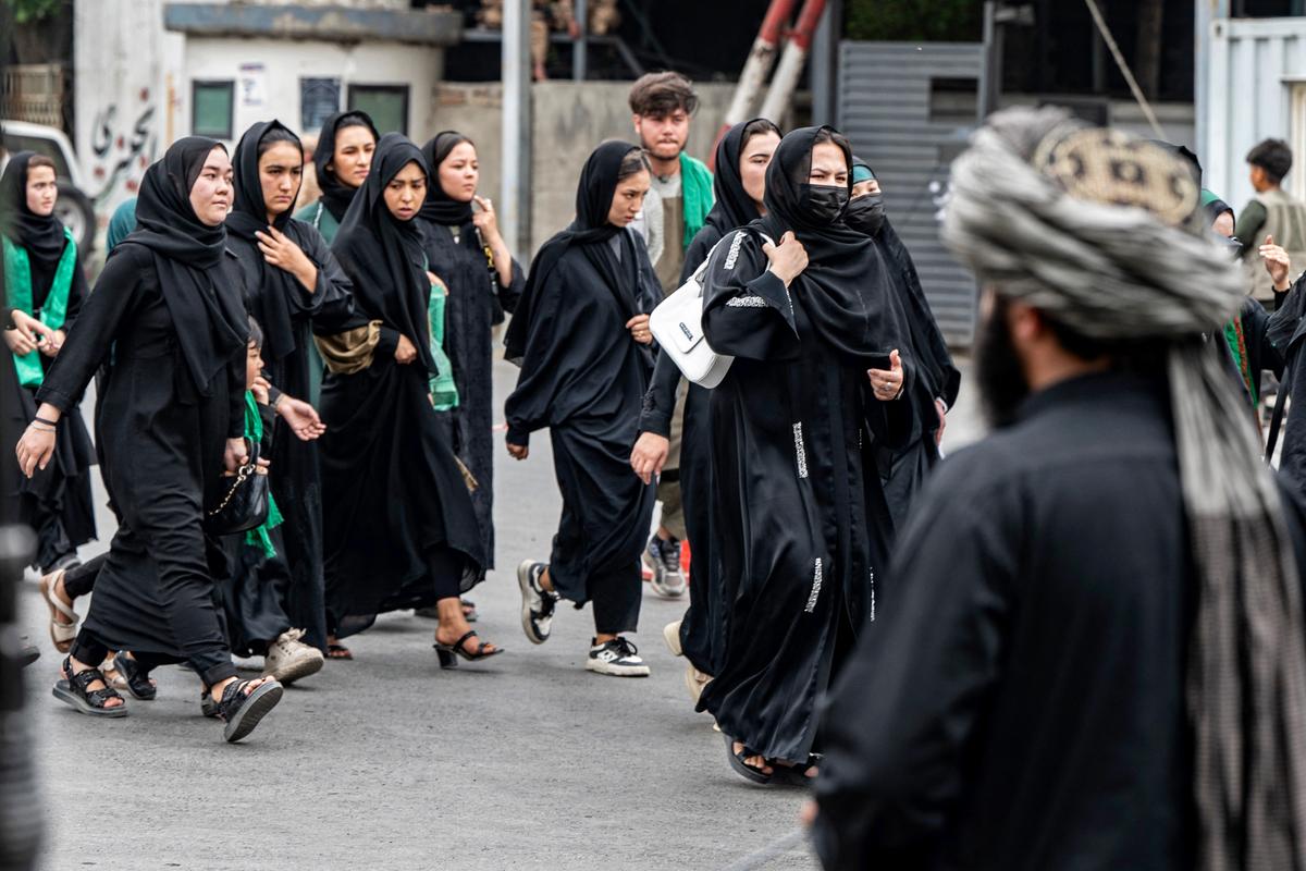 Un membre des forces de sécurité talibanes monte la garde tandis que des femmes musulmanes chiites afghanes défilent lors d'une procession religieuse organisée pour marquer l'Achoura, le dixième jour du mois sacré islamique de Muharram, à Kaboul, le 6 juillet 2025.