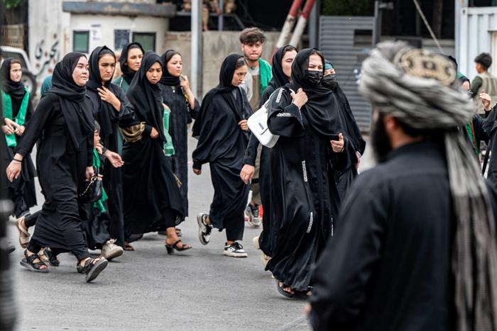 Un membre des forces de sécurité talibanes monte la garde tandis que des femmes musulmanes chiites afghanes défilent lors d'une procession religieuse organisée pour marquer l'Achoura, le dixième jour du mois sacré islamique de Muharram, à Kaboul, le 6 juillet 2025.